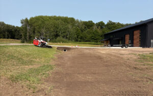 Excavation work with a compact track loader and freshly graded ground around a building.